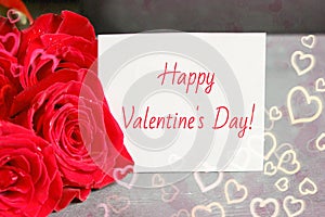 Bouquet of red roses and a sheet of white paper with a congratulation on Valentine`s day,