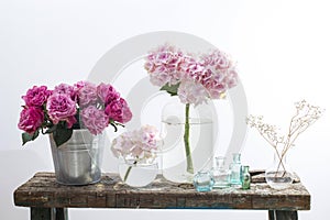 bouquet of red roses in tin bucket, multicolored pastel colored hydrangeas in a glass jar, gypsophila in a flask and a set of