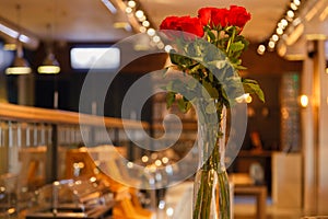 A bouquet of red roses in a transparent high vase stands on the