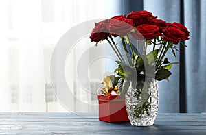 A bouquet of red roses in a vase and a gift box on the table. Love confession.