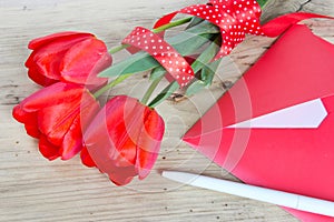 Bouquet of red tulips & envelope wooden background.