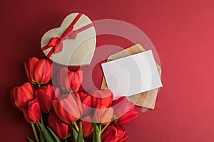 Bouquet of red  tulips and gift heart box isolated on red background . Spring flowers. Greeting card for Birthday, Woman, Mother`