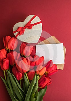 Bouquet of red  tulips and gift heart box isolated on red background . Spring flowers. Greeting card for Birthday, Woman, Mother`