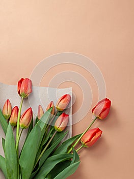 Bouquet of red tulips with kraft green envelope  on a natural beige color background. Mother`s Day, Easter, Valentine`s Day.