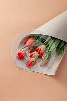 Bouquet of red tulips with kraft green envelope  on a natural beige color background. Mother`s Day, Easter, Valentine`s Day.