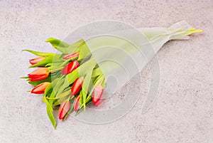 Bouquet of red tulips in  the package,  flowers in plastic wrap, romantic gift in cellophane on grey table, packed beautiful