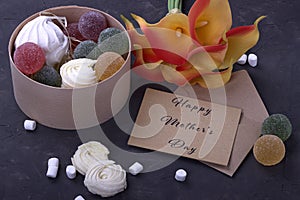 Bouquet of red yellow callas with marshmallows marmalade in a wooden round box and envelope with lettering Happy Mother`s Day on g