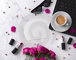 Bouquet of roses, cup of coffee, laptop, sunglasses and lipstick on white table.