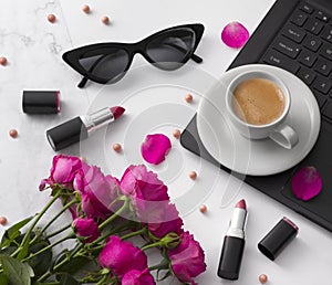 Bouquet of roses, cup of coffee, laptop, sunglasses and lipstick on white table.