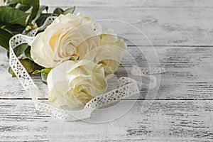 Bouquet of roses decorated with lace on white wooden background