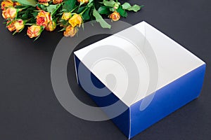 Bouquet of roses and open box lying in left corner of blue colored paper background