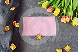 Bouquet of rosy and yellow tulips on a black abstract background, with dry petals. Space for text. Romance concept.