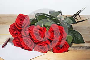 Bouquet of scarlet roses on a surface from wooden boards and the sheet paper for writing the text