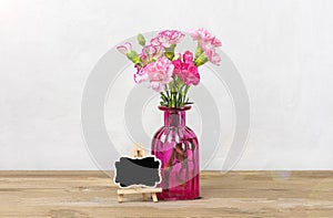 Bouquet of small colored pink carnations in vase, frame on wooden background and grey wall Hello spring, seasonal concept Mock up