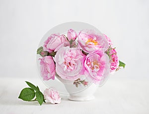 Bouquet of small light pink Roses in porcelain vase against of pale grey wooden background. Selective focus. Shallow depth of fiel