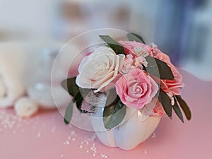 Bouquet of soap roses in vase, towel, cosmetic products on pink background.
