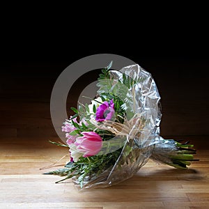 Bouquet of spring flowers in cellophane on wood, dark backgroun