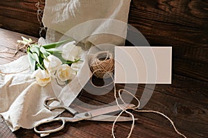 Bouquet of spring flowers on natural wooden table with blank greeting card, woman`s desk above view