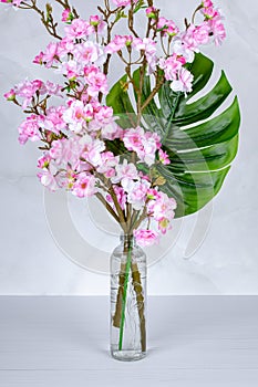A bouquet of spring flowers in a vase, pink cherry blossom in a glass bottle on a gray table. Home interior decor. Floral still