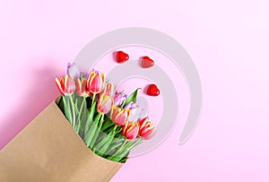 Bouquet of spring tulip flowers wrapped in craft paper bag on soft pink background