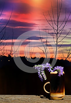 Bouquet of summer fragility flowers in wooden cup, rustic style and atmospheric mood. Dramatic sky and sunset landscape.