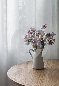 Bouquet of summer wildflowers in an enameled jug on a round wooden table