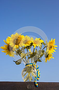 bouquet of sunflower flowers in a glass vase with a yellow - blue ribbon against the sky