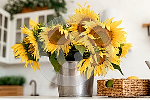 A bouquet of sunflowers stand on a white table in a bright kitchen.