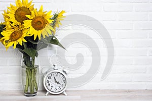 A bouquet of sunflowers in a vase and vintage alarm clock against the white brick wall