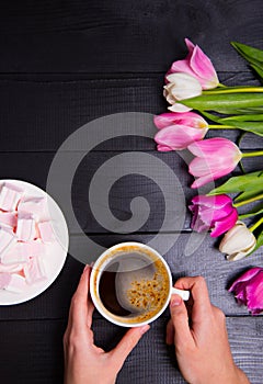 Bouquet of tender pink tulips and hands holding cup of coffee an