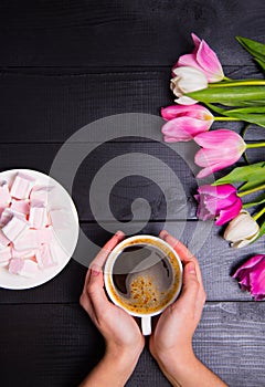 Bouquet of tender pink tulips and hands holding cup of coffee an