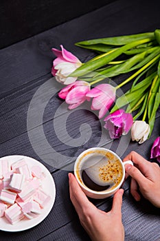 Bouquet of tender pink tulips and hands holding cup of coffee an