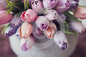 Bouquet of tulip flowers. Spring flower decoration. Violet, purple, orange and pink tulips on grey tabouret.