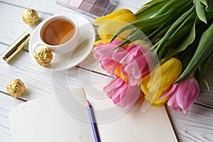 A bouquet of tulips, a cup of tea, some sweets, a note book, some jewellery, eye