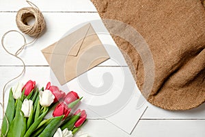 Bouquet of tulips flowers, kraft envelope, twine, burlap on white wooden table. Vintage greeting card for womans day, mothers day,