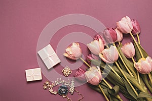 A bouquet of tulips and a necklace as a gift for the holiday. Beautiful flowers on a pink background