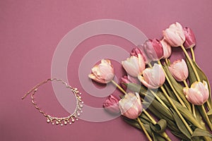 A bouquet of tulips and a necklace as a gift for the holiday. Beautiful flowers on a pink background. Holidays concept - mother`s