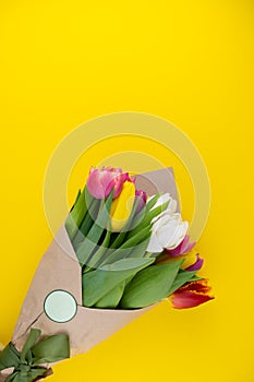 A bouquet of tulips wrapped in craft paper. Spring flowers. Gift delivery. Celebration. Copy space. Yellow, white, pink, purple