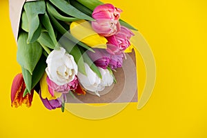 A bouquet of tulips wrapped in craft paper. Spring flowers. Gift delivery. Celebration. Copy space. Yellow, white, pink, purple
