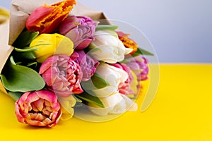 A bouquet of tulips wrapped in craft paper. Spring flowers. Gift delivery. Celebration. Copy space. Yellow, white, pink, purple