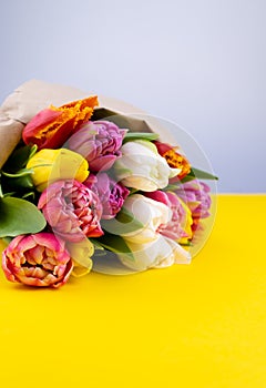 A bouquet of tulips wrapped in craft paper. Spring flowers. Gift delivery. Celebration. Copy space. Yellow, white, pink, purple