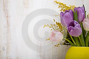 Bouquet of tulips in a yellow vase on a wooden background.