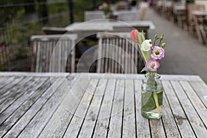 bouquet of two pink lisianthus, a red tulip and a white rose on a wooden table in a glass vase in a street cafe