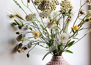 Bouquet of various wildflowers in a pink vase in home interior. Cosy atmosphere.