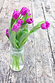 Bouquet of violet tulips on the oak brown table in a clear glass jar