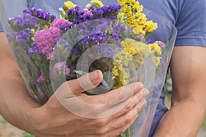 Bouquet of violet, yellow, pink and white statis in the man`s hands