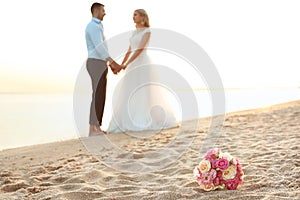 Bouquet and wedding couple on beach.