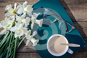 A bouquet of white daffodils, book, glasses and a cup of coffee with milk