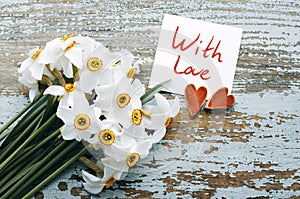 Bouquet of white daffodils, two decorative hearts and a card with the inscription WITH LOVE on the background of an old wooden sur