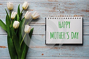 Bouquet of white flowers of tulips on the background of blue boards with a notebook with lettering Happy Mother`s Day